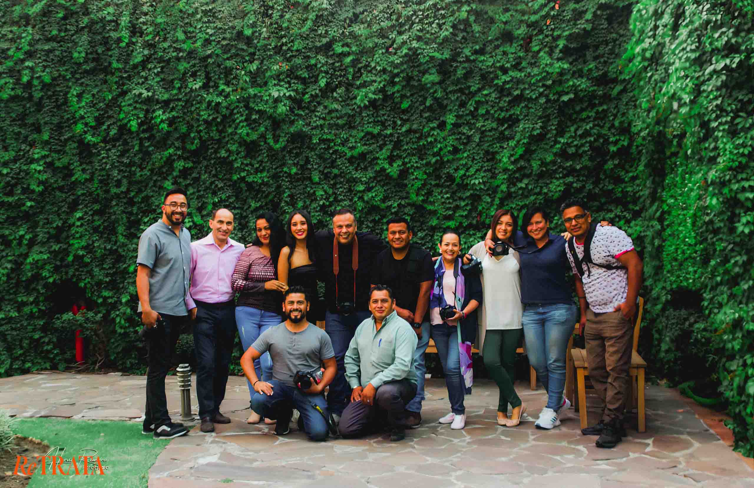 Foto grupal a color de los asistentes al curso de fotografía RETRATA en Puebla, Junio 2023, posando frente a un muro verde.